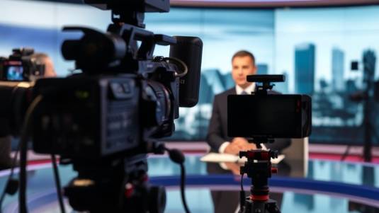 Anchor at news desk talking into camera, behind the scenes shot.